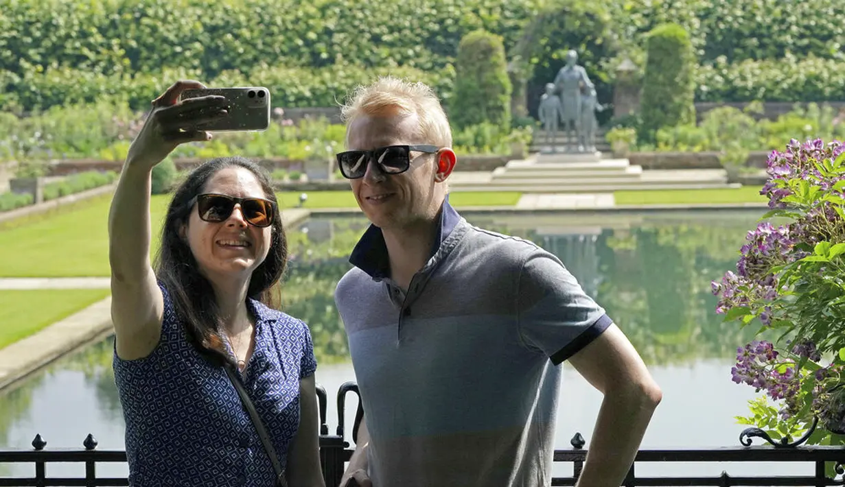 Sepasang suami istri berfoto selfie saat melihat patung Diana, Princess of Wales, sehari setelah pembukaannya, di Taman Sunken di Istana Kensington, London, Jumat (2/7/2021). (Jonathan Brady/Pool Photo via AP)