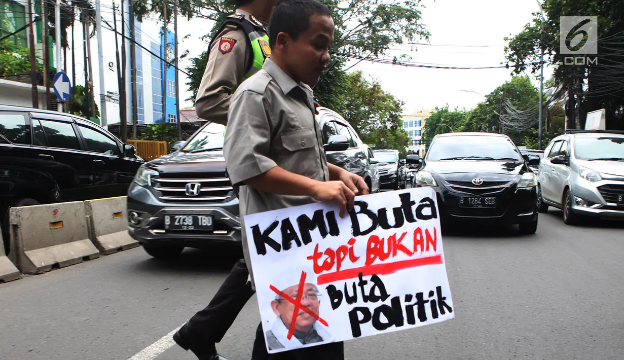 Seorang petugas polisi membantu penyandang disabilitas PASTI menyebrangi  jalan saat menggelar aksi di depan kantor Majelis Ulama Indonesia (MUI), Jakarta Pusat, Rabu (14/11). (Merdeka.com/Imam Buhori)
