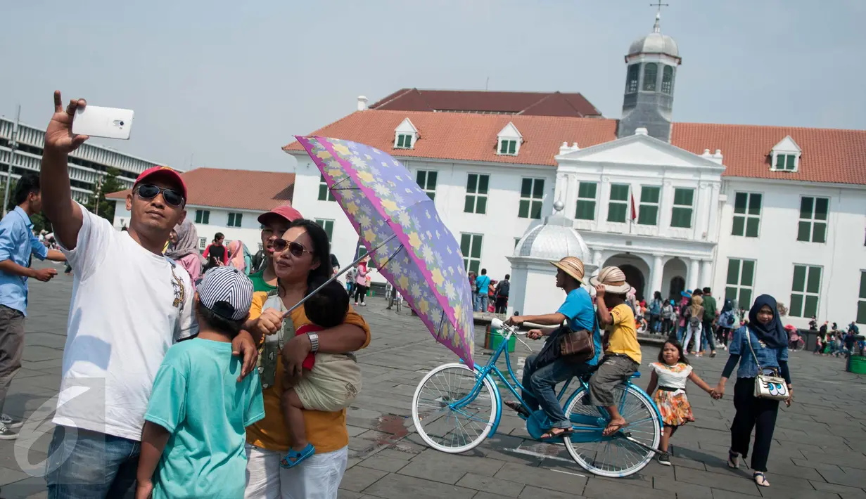 Warga berpose dengan latar Gedung Fatahillah di kawasan Kota Tua, Jakarta, Senin (5/1). Kota Tua masih menjadi tempat pilihan untuk warga Jakarta dan sekitarnya mengisi waktu libur. (Liputan6.com/Gempur M Surya)