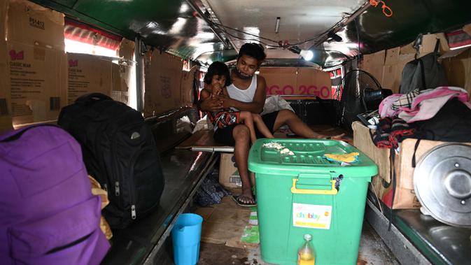 Daniel Flores bersama salah satu anaknya di dalam jeepney mereka yang berfungsi sebagai rumah sementara di Manila, 12 Agustus 2020. Angkutan ikonik di Filipina itu belum dapat mengangkut penumpang sejak Maret akibat lockdown Covid-19 yang membuat jutaan orang kehilangan pekerjaan. (Ted ALJIBE/AFP)