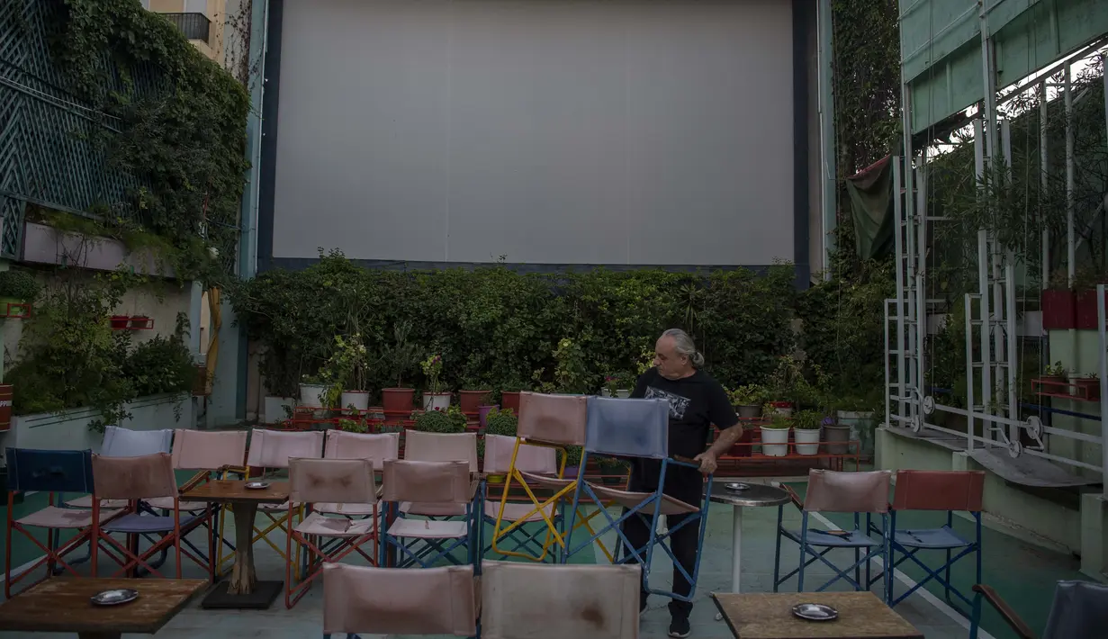 Seorang pegawai menata kursi sebelum pemutaran film di bioskop terbuka Palace, Athena, Yunani, 10 Agustus 2020. Pandemi COVID-19 memaksa bioskop terbuka dipersingkat sehingga menyebabkan penurunan jumlah penonton. (ANGELOS TZORTZINIS/AFP)