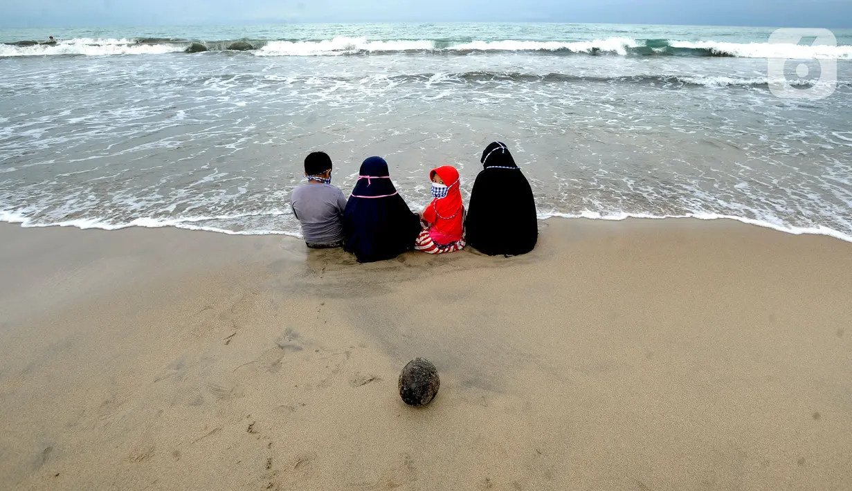 Wisatawan yang mengenakan masker menikmati suasana Pantai Anyer di Cilegon, Banten, Minggu (25/10/2020). Akhir pekan dimanfaatkan warga Jakarta dan sekitarnya untuk berwisata dengan tetap menerapkan protokol kesehatan Covid-19. (merdeka.com/Arie Basuki)