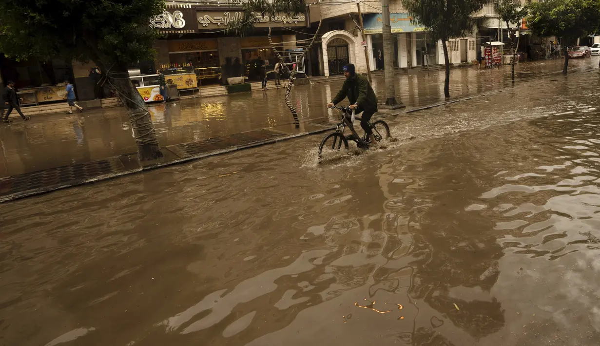 Seorang pemuda mengendarai sepedanya di jalan yang banjir saat hujan lebat di Kota Gaza, Selasa (8/11/2022). Hujan deras menyebabkan banjir bandang di Jalur Gaza pada hari Selasa, di mana infrastruktur yang bobrok sering membuat air banjir tidak surut, memperpanjang kerusakan. (AP Photo/Adel Hana)