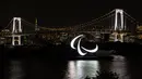Simbol Paralimpiade menyala pada malam hari dengan latar belakang Jembatan Pelangi dan Menara Tokyo di tepi Pantai Odaiba, Tokyo, Jepang, 23 Agustus 2021. Paralimpiade Tokyo 2020 mulai 24 Agustus 2021 sampai 5 September 2021. (Charly TRIBALLEAU/AFP)