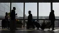 Pelancong berjalan dengan barang bawaan mereka di Bandara Ben Gurion dekat Tel Aviv, Minggu (28/11/2021). Israel pada Minggu menyetujui larangan masuknya warga negara asing dan penggunaan teknologi kontroversial untuk pelacakan kontak guna menekan penyebaran varian Omicron. (AP Photo/Ariel Schalit)