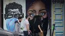 Pejalan kaki yang mengenakan masker melewati mural yang dilukis pada bisnis papan di pusat kota Austin, Texas, Selasa (9/3/2021). Mandat Gubernur Texas Greg Abbott yang mencabut keharusan mengenakan masker di negara bagiannya akan berlaku penuh mulai 10 Maret. (AP Photo/Eric Gay)