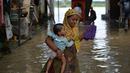 Seorang wanita membawa seorang anak saat melintasi banjir di daerah perumahan dekat tepi Sungai Yamuna yang meluap di New Delhi, India, Selasa (20/8/2019). (AFP Photo/Sajjad Hussain)