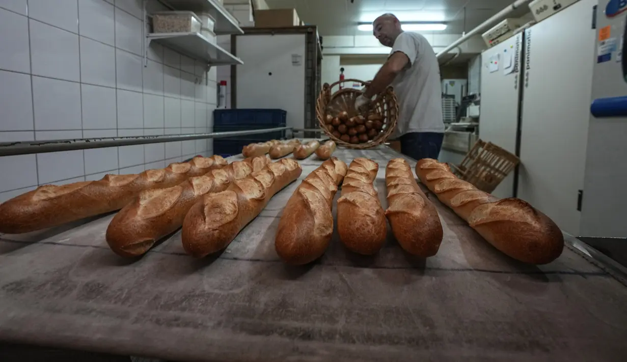 Baker David Buelens memasukkan baguette ke dalam keranjang di sebuah toko roti, di Versailles, sebelah barat Paris, Selasa, 29 November 2022. Roti, yang disebut Presiden Prancis Emmanuel Macron sebagai "250 gram keajaiban dan kesempurnaan," telah jadi bagian klasik kehidupan warga negara itu. (AP Photo/Michel Euler)