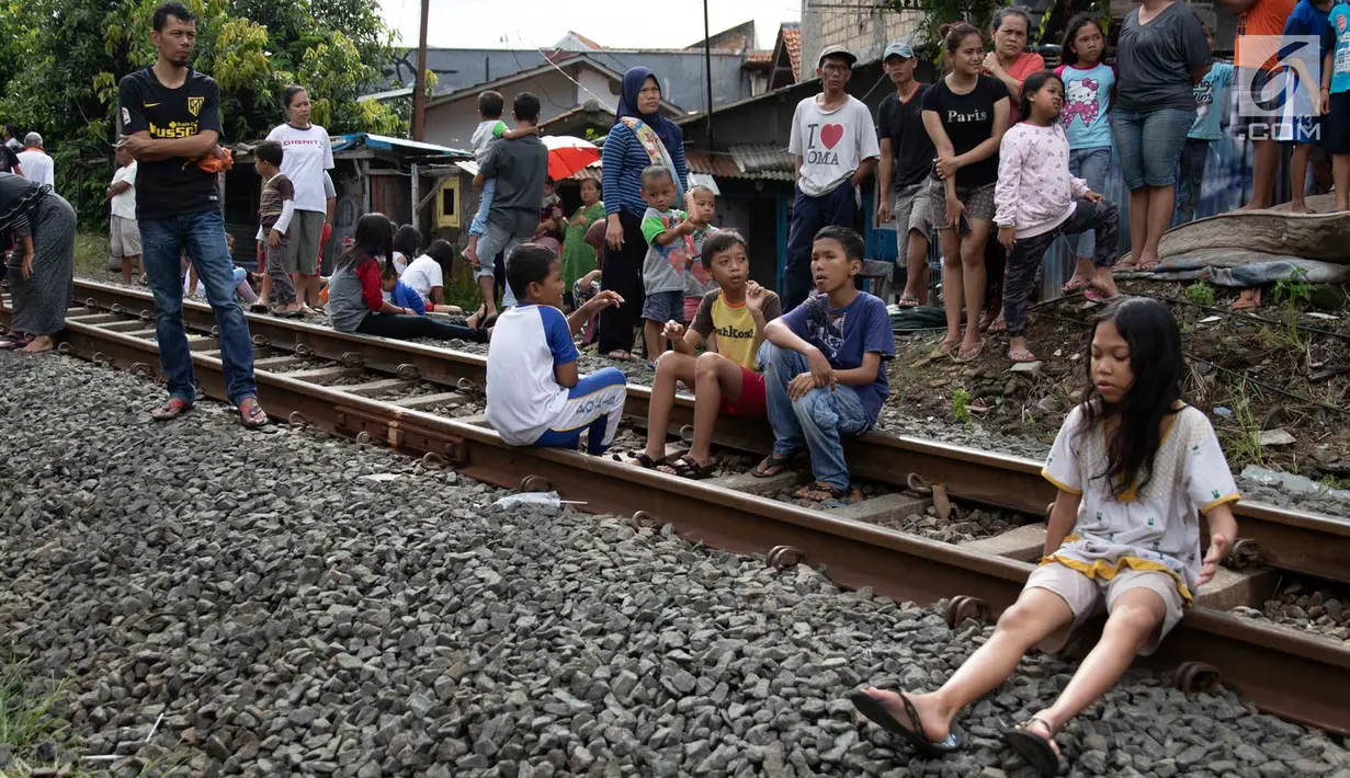 Warga duduk di rel saat melihat proses evakuasi KRL yang anjlok di kawasan Kebon Pedes, Bogor, Jawa Barat, Minggu (10/3). Penanganan KRL anjlok dilakukan dengan menggunakan crane yang didatangkan dari Bandung. (Liputan6.com/Immanuel Antonius)