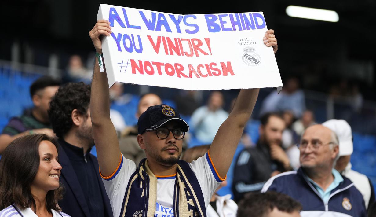 Seorang pendukung Real Madrid membawa poster bertuliskan "Selalu di belakangmu Vini Jr!" pada laga lanjutan Liga Spanyol 2022/2023 antara Real Madrid melawan Rayo Vallecano pada Kamis (25/05/2023) dini hari WIB. Los Blancos memberikan aksi solidaritas sebelum laga tersebut setelah pemain Brasil itu menjadi korban rasisme pada Minggu (21/05/2023) lalu. (AP Photo/Manu Fernandez)