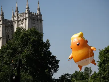 Balon raksasa berbentuk bayi menyerupai Presiden AS, Donald Trump melayang dekat menara Westminster Abbey selama demonstrasi di Parliament Square, London, Jumat (13/7). Puluhan ribu orang menggelar aksi damai menentang kedatangan Trump. (AFP/TolgaAKMEN)