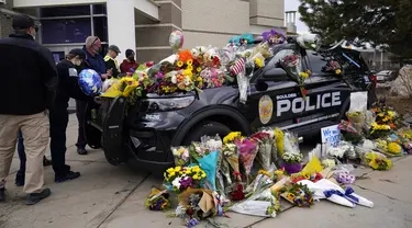 Warga meninggalkan karangan bunga di mobil polisi yang diparkir di luar Departemen Kepolisian Boulder setelah seorang petugas menjadi salah satu korban penembakan massal di toko King Soopers di Boulder, Colorado (23/3/2021). (AP Photo/David Zalubowski)