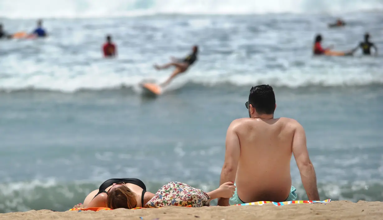 <p>Dua turis berjemur di pantai Kuta di pulau pariwisata Indonesia di Bali (4/1). Sebelum menjadi objek wisata, Kuta merupakan sebuah pelabuhan dagang tempat produk lokal diperdagangkan kepada pembeli dari luar Bali. (AFP Photo/Sony Tunbelaka)</p>
