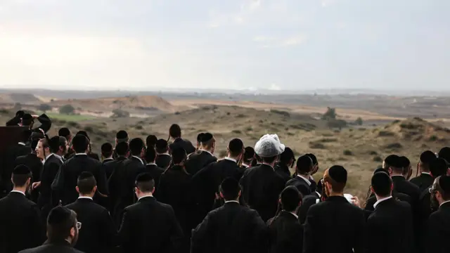 Pria Yahudi ultra-Ortodoks Israel berkumpul di sebuah bukit di kota selatan Sderot, dan menyaksikan pasukan Israel membombardir Jalur Gaza utara.