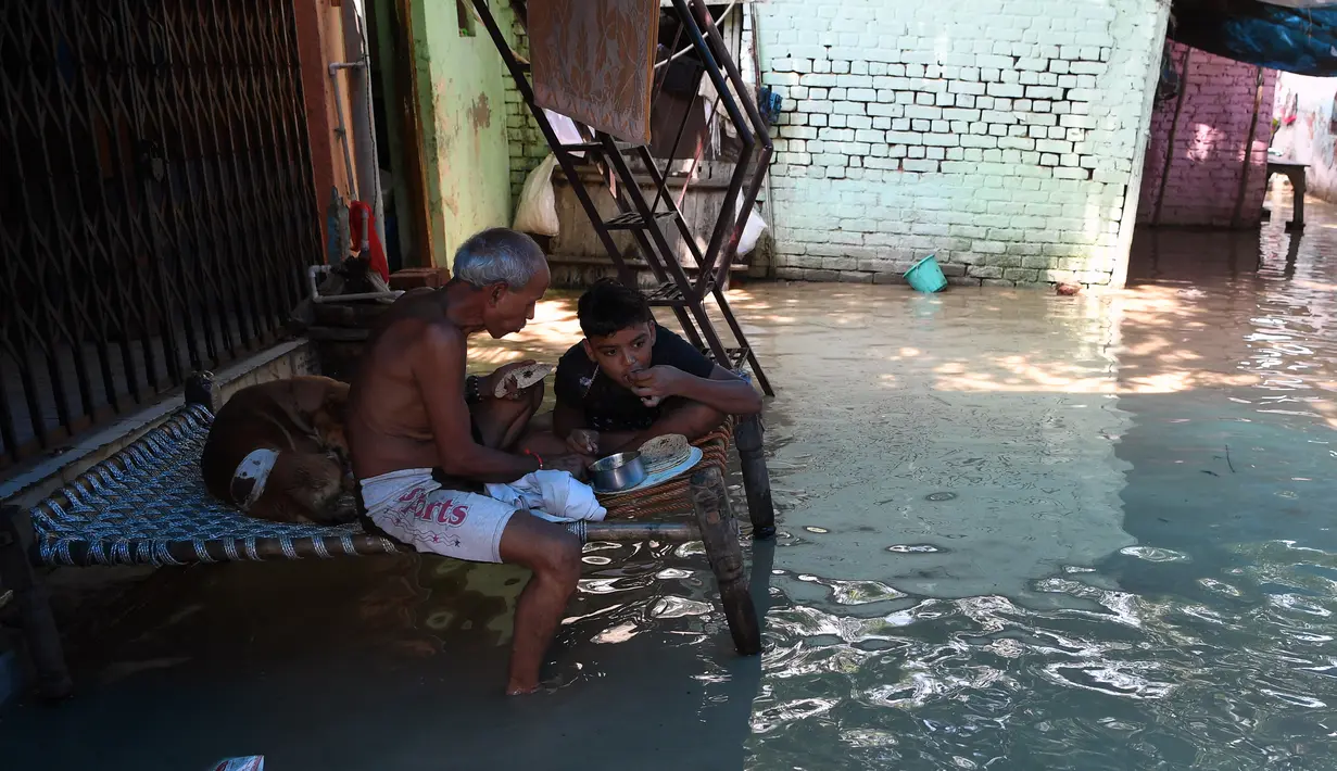 Seorang pria dan anak laki-laki makan di atas bangku saat banjir melanda daerah perumahan dekat tepi Sungai Yamuna yang meluap di New Delhi, India, Selasa (20/8/2019). (AFP Photo/Sajjad Hussain)