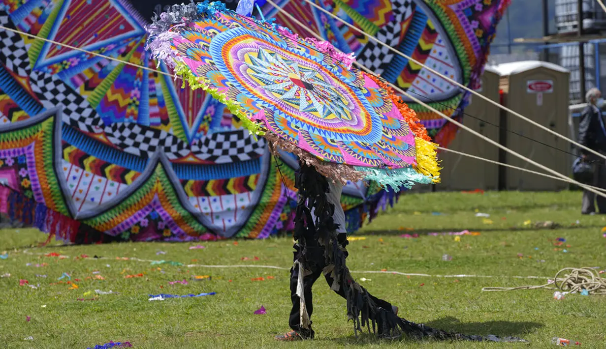Seorang pria membawa layang-layang besar untuk ditampilkan pada Hari Semua Orang Kudus sebagai bagian dari perayaan Hari Kematian di Santiago Sacatepequez, Guatemala, 1 November 2021. Perayaan digelar dengan sejumlah pembatasan untuk mengekang penyebaran COVID-19. (AP Photo/Moises Castillo)