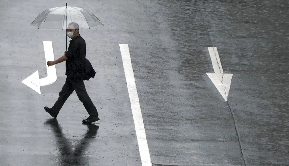 Seorang pria menyeberang jalan di tengah hujan dari Topan Mindulle di Tokyo, Jepang, Jumat (1/10/2021). Topan Mindulle sedang bergerak di lepas pantai Jepang. (AP Photo/Eugene Hoshiko)