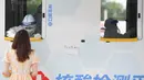 Petugas medis mengambil sampel usap tenggorokan seorang wanita dari sebuah kendaraan tes mobile yang baru diadopsi di Distrik Xicheng, Beijing, China, Minggu (28/6/2020). (Xinhua/Ju Huanzong)