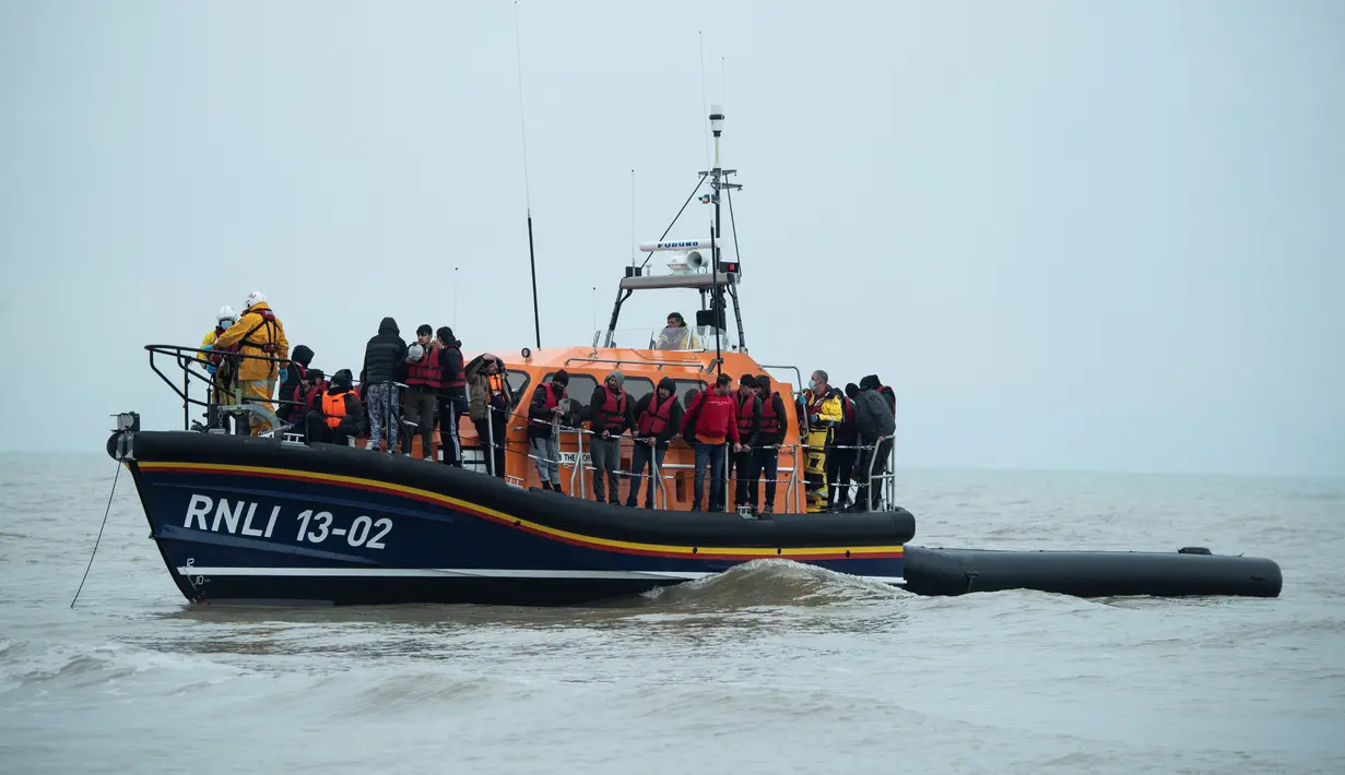 Para migran berdiri di atas sekoci RNLI (Royal National Lifeboat Institution) setelah diselamatkan saat menyeberangi Selat Inggris di lepas pantai di Dungeness, Inggris tenggara (24/11/2021). (AFP/Ben Stansall)