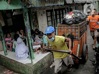 Warga membawa gerobak sampah melintas saat sejumlah murid SD mengikuti kegiatan pembelajaran jarak jauh di sebuah pos keamanan RT 003 RW 006 Bendungan Hilir, Tanah Abang, Jakarta, Jumat (14/8/2020). (Liputan6.com/Faizal Fanani)