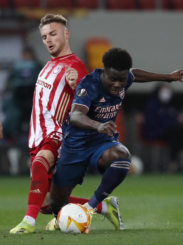 Gelandang Arsenal, Bukayo Saka berebut bola dengan gelandang Olympiakos, Andreas Bouchalakis pada pertandingan leg pertama babak 16 besar Liga Europa di stadion Georgios Karaiskakis, Athena, Jumat (12/3/2021). Arsenal menang atas Olympiakos 3-1. (AP Photo/Thanassis Stavrakis)