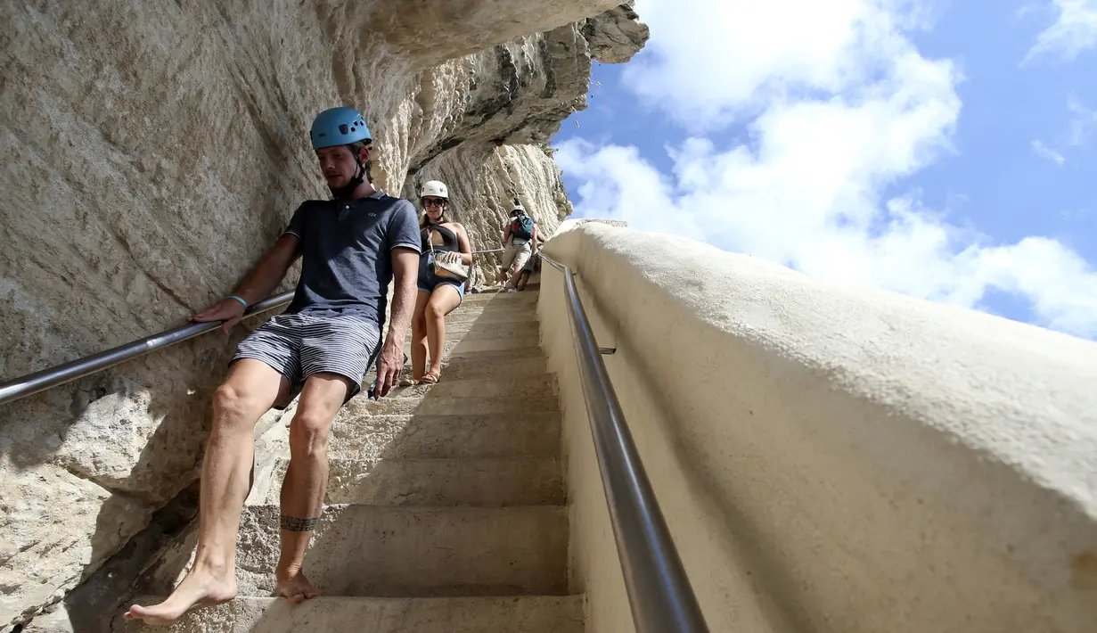 Turis menuruni tangga Raja Aragon di Bonifacio di pulau Corsica, Mediterania Prancis (19/9/2021). Menurut legendanya, Tangga Raja Aragon, sebuah monumen bersejarah Corsica, digali dengan tangan di tebing batu kapur di suatu malam oleh pasukan Raja Aragon tahun 1420. (AFP/Pascal Pochard-Casabianca)