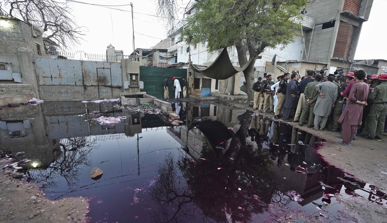 Petugas polisi dan awak media berkumpul di lokasi penyerbuan mematikan di pusat distribusi makanan dan sedekah Ramadhan di kota pelabuhan Karachi, Pakistan selatan, Jumat, 31 Maret 2023. (AP Photo/Fareed Khan)