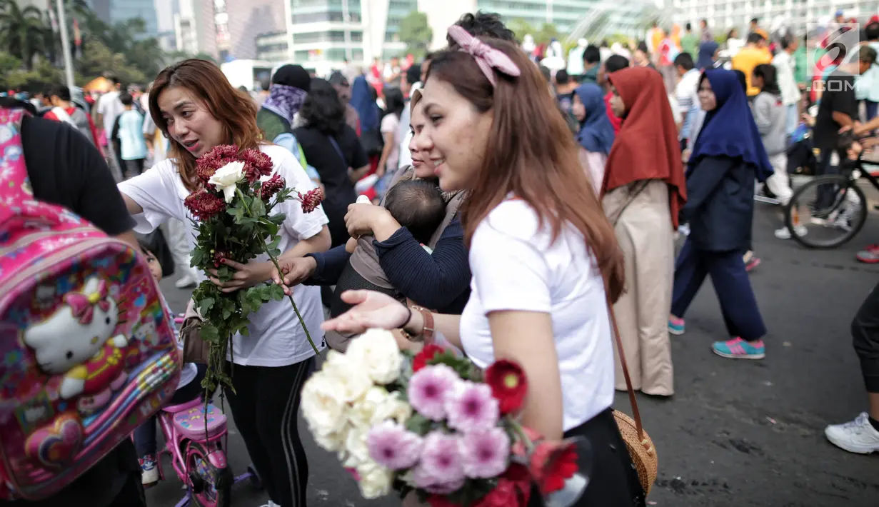 Anggota TKN Milenial Jokowi-Ma'ruf membagikan bunga kepada pengunjung car free day dalam kegiatan tabur bunga di Bundaran HI, Jakarta, Minggu (28/4/2019). Mereka mengajak masyarakat untuk ikut mengungkapkan duka atas meninggalnya 272 petugas KPPS dalam Pemilu 2019. (Liputan6.com/Faizal Fanani)