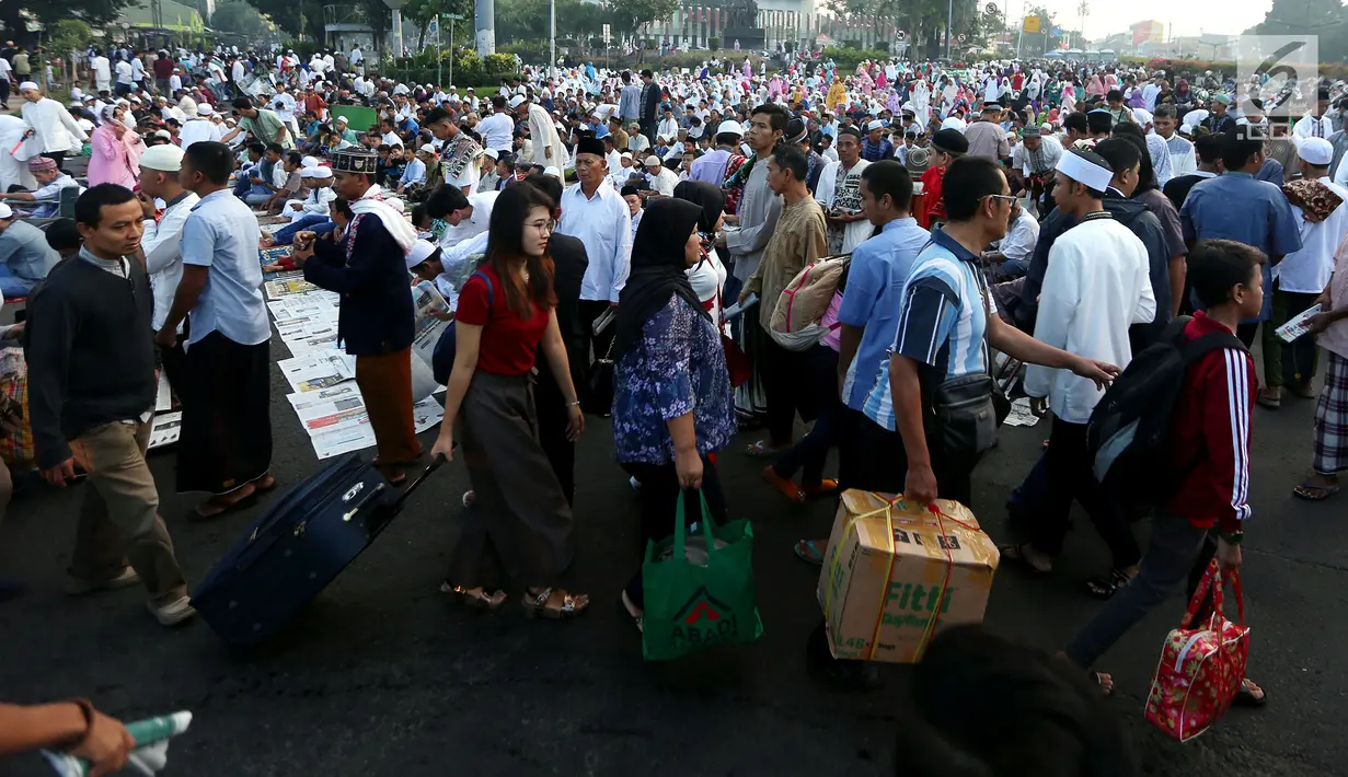 Pemudik melewati umat muslim yang baru saja melaksanakan Salat Idul Fitri di kawasan Senen, Minggu (25/6). Hari Raya Idul Fitri 1438 H disambut umat muslim dengan melaksanakan salat Ied di masjid-masjid dan tempat terbuka. (Liputan6.com/Johan Tallo)