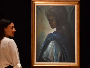 Karyawan rumah lelang Bonhams berpose dekat lukisan seorang putri Nigeria bernama Tutu di London, Inggris pada 7 Februari 2018. Lukisan yang kerap disebut ‘Mona Lisa dari Afrika’ itu terjual dalam sebuah lelang pada 28 Februari 2018. (BEN STANSALL/AFP)