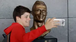 Seorang anak berswafoto dengan patung Cristiano Ronaldo di bandara internasional Madeira di Funchal, Portugal, Rabu (29/3). Bukan kali ini saja Ronaldo menjadi bahan ejekan, patung di bandara Madeira ini tidak mirip dengannya. (AP Photo/Armando Franca)