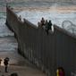 Dua imigran Honduras mengangkangi perbatasan yang memisahkan Meksiko dari AS di Tijuana, Meksiko, Rabu (21/11). Wali Kota Tijuana mendeklarasikan krisis kemanusiaan di perbatasan kotanya dengan AS. (AP Photo/Ramon Espinosa)