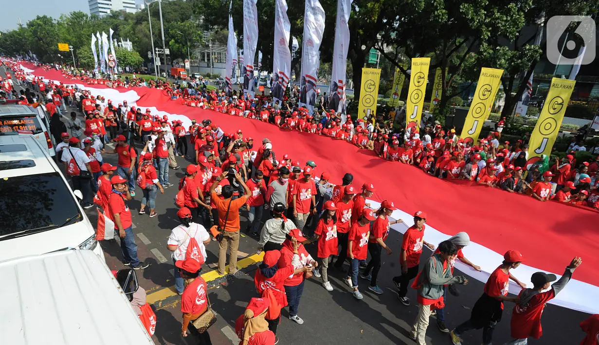 Relawan Jokowi-Ma'ruf Amin membawa bendera raksasa sepanjang sekitar 200 meter saat menyambut pelantikan Presiden-Wapres terpilih periode 2019-2024 di sekitar Patung Kuda, Jakarta, Minggu (20/10/2019). (merdeka.com/Arie Basuki)