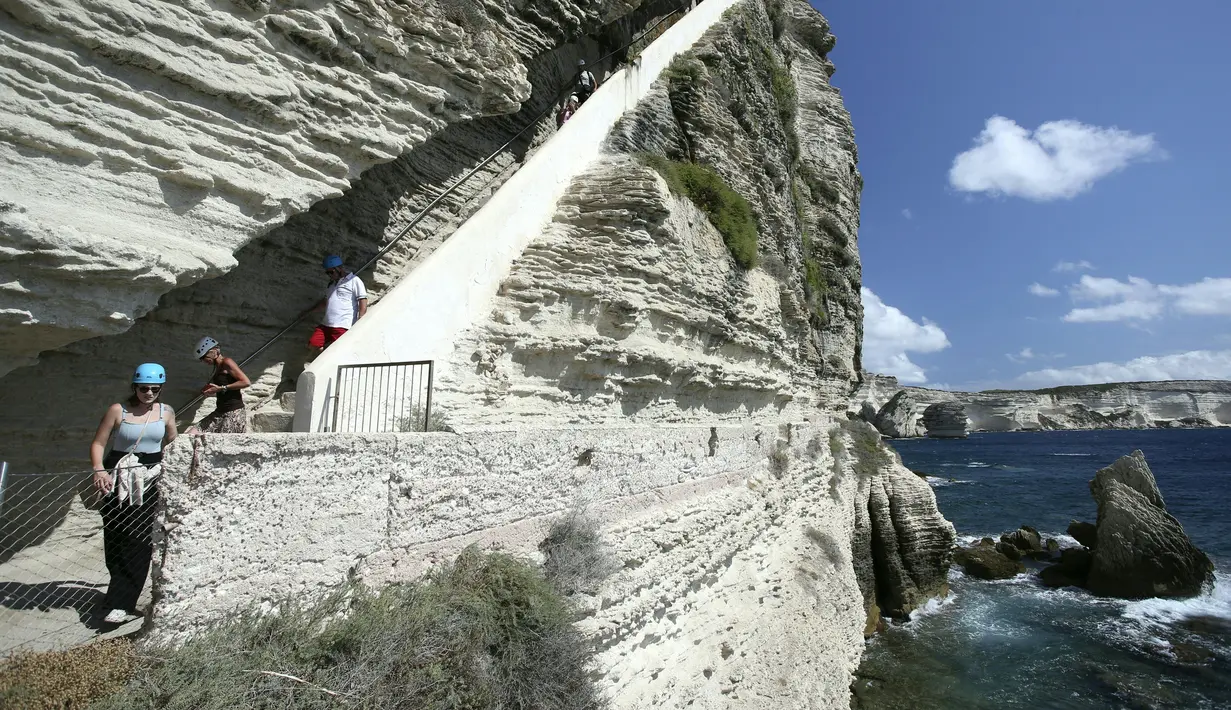 Turis menuruni tangga Raja Aragon di Bonifacio di pulau Corsica, Mediterania Prancis (19/9/2021). Menurut legendanya, Tangga Raja Aragon, sebuah monumen bersejarah Corsica, digali dengan tangan di tebing batu kapur di suatu malam oleh pasukan Raja Aragon tahun 1420. (AFP/Pascal Pochard-Casabianca)