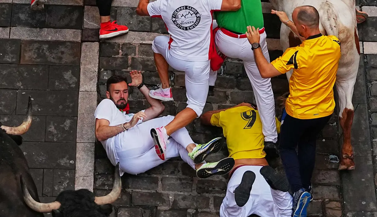 Para pengunjung berlari dan terjatuh di samping banteng-banteng petarung Victoriano del Río selama acara lari banteng ketiga di festival San Fermín di Pamplona, Spanyol, Kamis, 9 Juli 2026. (AP Photo/Miguel Oses)