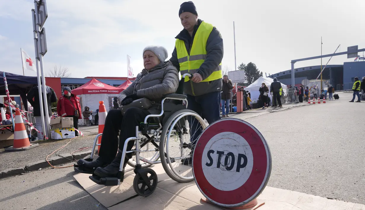 Seorang pria mendorong seorang perempuan di kursi roda melintasi perbatasan di Vysne Nemecke, Slovakia, 3 Maret 2022. Badan pengungsi PBB , UNHCR pada Kamis (3/3) melaporkan 1 juta orang telah meninggalkan Ukraina sejak invasi Rusia sepekan lalu. (AP Photo Darko Vojinovic)