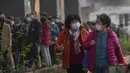 Dua wanita berbincang sambil melewati warga yang antre menerima suntikan booster di tempat vaksinasi di Beijing, Senin (25/10/2021). Sebuah provinsi di China barat laut yang bergantung pada pariwisata menutup semua lokasi wisata pada Senin usai menemukan kasus baru COVID-19. (AP Photo/Andy Wong)