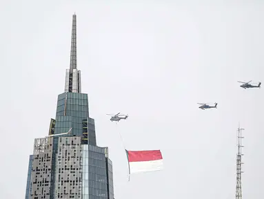 Helikopter TNI AU mengibarkan bendera Merah Putih raksasa di kawasan Gedung DPR RI, Jakarta, Selasa (5/10/2021). TNI AU mengerahkan enam helikopter yang membawa bendera Merah Putih serta bendera Trimatra raksasa. (Liputan6.com/Faizal Fanani)