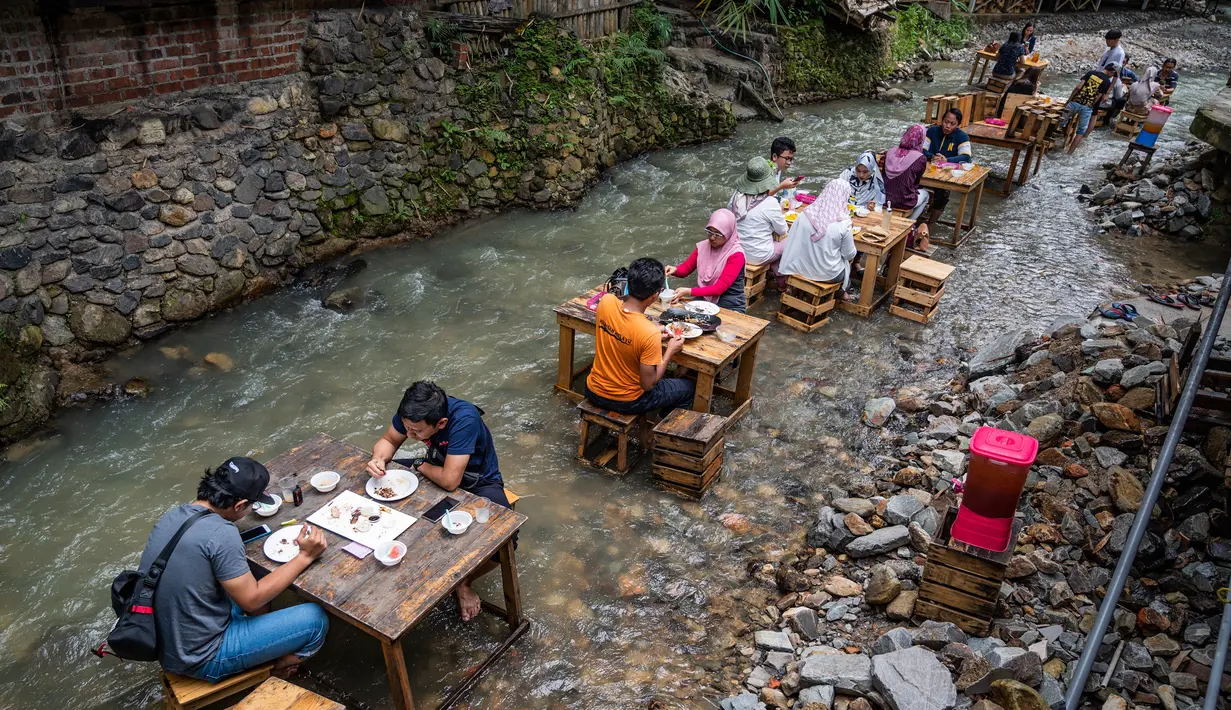 Pelanggan menikmati makan siang di sebuah restoran dengan meja yang berada di tengah aliran sungai di Kampung Kemensah di pinggiran Kuala Lumpur, Malaysia, Selasa (14/7/2020). Tak perlu khawatir, air sungai yang datang dari bukit ini masih bersih dan menyegarkan. (Photo by Mohd RASFAN / AFP)