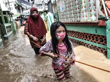 Seorang anak dan wanita berpegangan pada tali saat menyusuri banjir yang merendam permukiman di Kebon Pala, Jakarta, Senin (8/2/2021). Hujan deras yang mengguyur Ibu Kota dan Bogor menyebabkan permukiman di Kebon Pala terendam banjir sejak Minggu (7/2/2021) sore. (merdeka.com/Iqbal S. Nugroho)