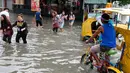 Warga berjalan di antara banjir yang terjadi di Metropolitan Manila, Filipina, Jumat (20/7). Banjir diakibatkan hujan musim angin barat daya yang dibawa oleh badai tropis. (AP Phoyo/Aaron Favila)