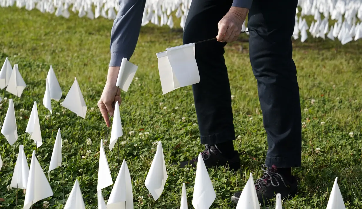 Relawan memancangkan bendera putih ke instalasi seni sementara untuk mengenang warga Amerika yang meninggal karena COVID-19 di dekat Stadion RFK di Washington, Selasa (27/10/2020). Instalasi seni Suzanne Brennan Firstenberg itu disebut "In America, How Could This Happen.” (AP/Patrick Semansky)