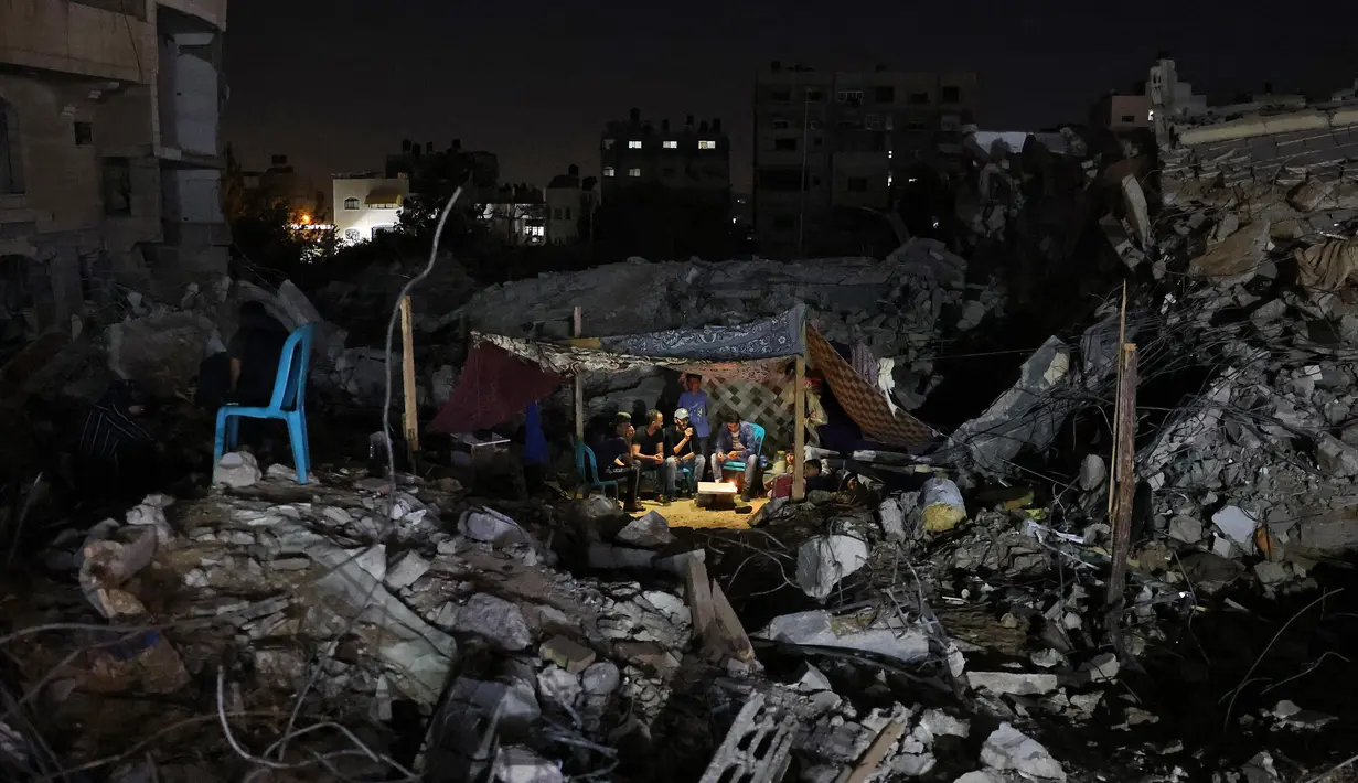 Warga Palestina duduk di tenda yang didirikan di atas reruntuhan bangunan yang hancur dalam serangan udara Israel di Kota Gaza (24/5/2021). Sementara itu, roket dari Gaza merenggut 12 nyawa di Israel, termasuk satu anak dan seorang tentara Israel. (AFP/Mohamed Abed)