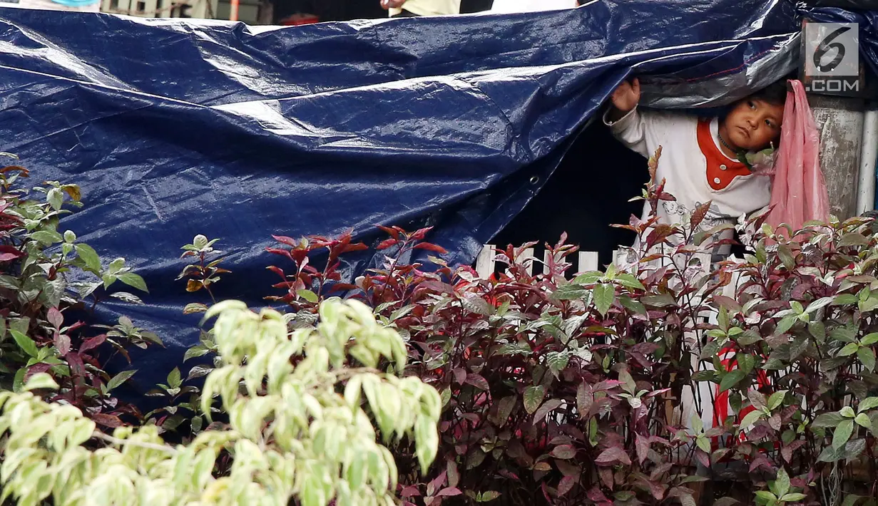 Seorang bocah pencari suaka menengok dari balik terpal di trotoar depan Rumah Detensi Imigrasi Kalideres, Jakarta, Jumat (19/1). Sebanyak 57 WNA tinggal di trotoar karena ruangan Rumah Detensi Imigrasi tersebut penuh. (Liputan6.com/JohanTallo)