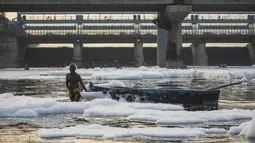 Seorang pria menarik perahu di tengah busa di sungai Yamuna yang tercemar di pinggiran New Delhi (23/7/2020). Sungai yang sangat dianggap suci oleh umat Hindu India ini masih tercemar, salah satunya akibat busa polusi memenuhinya. (AFP Photo/Xavier Galiana)