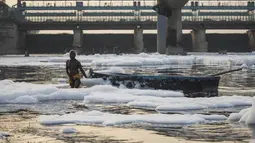 Seorang pria menarik perahu di tengah busa di sungai Yamuna yang tercemar di pinggiran New Delhi (23/7/2020). Sungai yang sangat dianggap suci oleh umat Hindu India ini masih tercemar, salah satunya akibat busa polusi memenuhinya. (AFP Photo/Xavier Galiana)