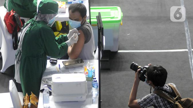 Fotografer mengambil gambar seorang jurnalis yang menjalani penyuntikkan vaksin COVID-19 di Hall A Basket Gelora Bung Karno, Senayan, Kamis (25/2/2021). Sekitar 5.500 jurnalis yang akan mendapatkan vaksin COVID-19  selama tiga hari pelaksanaan vaksinasi. (merdeka.com/Arie Basuki)