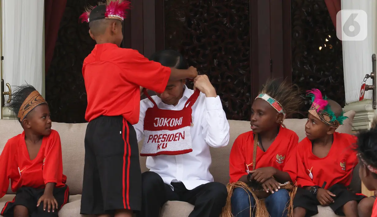 Presiden Joko Widodo atau Jokowi mendapatkan hadiah dari perwakilan anak-anak sekolah dasar Papua di Istana Merdeka, Jakarta, Jumat (11/10/2019). Pertemuan Jokowi dengan perwakilan anak-anak SD dari Papua digelar dalam suasana santai di beranda belakang Istana Merdeka. (Liputan6.com/Angga Yuniar)