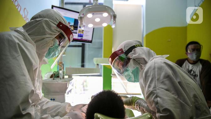 Dokter menggunakan APD memeriksa gigi pasien anak di klinik Medikids kawasan Kemang, Jakarta Selatan, Selasa (7/7/2020). Pelayanan dokter gigi dengan menggunakan APD lengkap untuk memenuhi protokol kesehatan guna mencegah penyebaran covid-19 di era kenormalan baru. (Liputan6.com/Faizal Fanani)