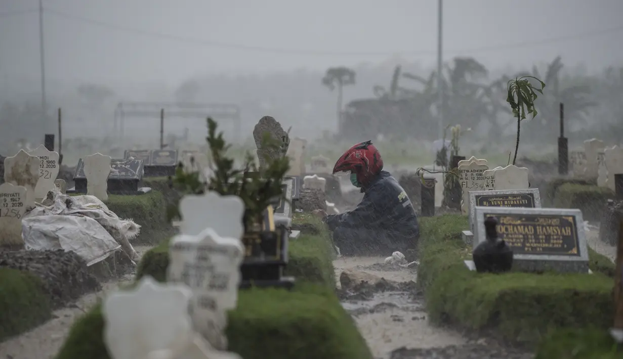 Seorang warga berdoa di tengah hujan deras di makam keluarganya di lahan khusus korban Covid-19 di TPU Keputih, Surabaya, Jawa Timur, Kamis (7/1/2020). Total sembuh 17.006 dan 1.256 meninggal dunia. (AFP/Juni Kriswanto)